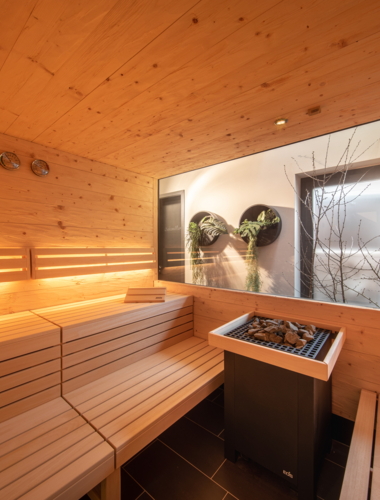 Ein moderner Saunaraum mit Holzverkleidung und sanfter Beleuchtung. Durch das große Fenster blickt man ins Freie auf eine ruhige Natur.