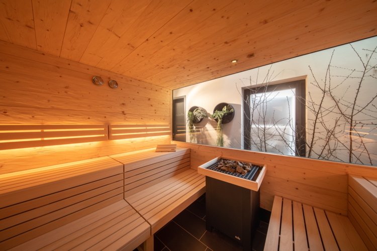 Ein moderner Saunaraum mit Holzverkleidung und sanfter Beleuchtung. Durch das große Fenster blickt man ins Freie auf eine ruhige Natur.